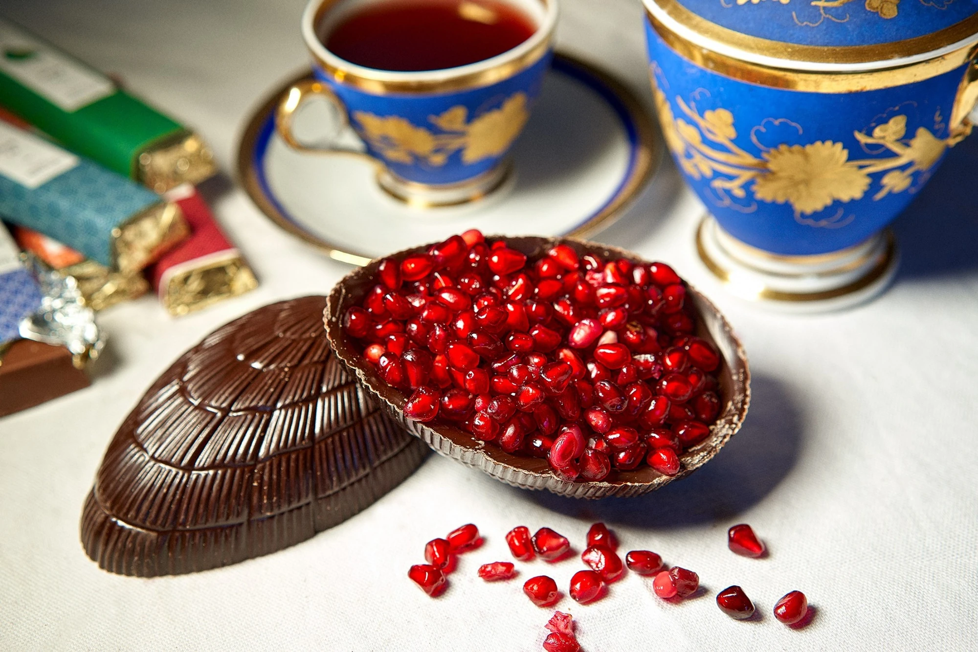 Œuf en chocolat garni de graines de grenade, posé avec tasses bleues et or